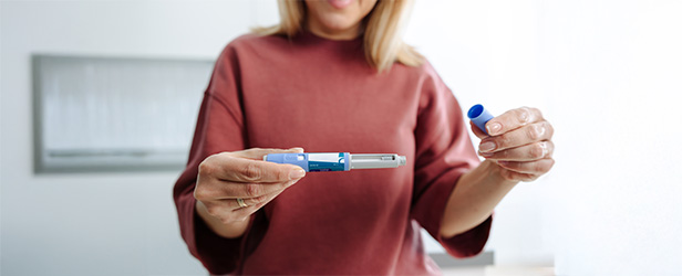 A woman holds a GLP-1 Injection pen with the cap off.