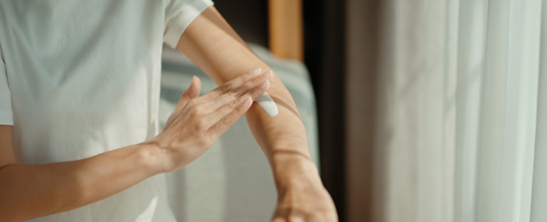 Person putting sunblock on their arm indoors.
