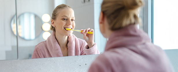Woman brushes teeth while looking in mirror.